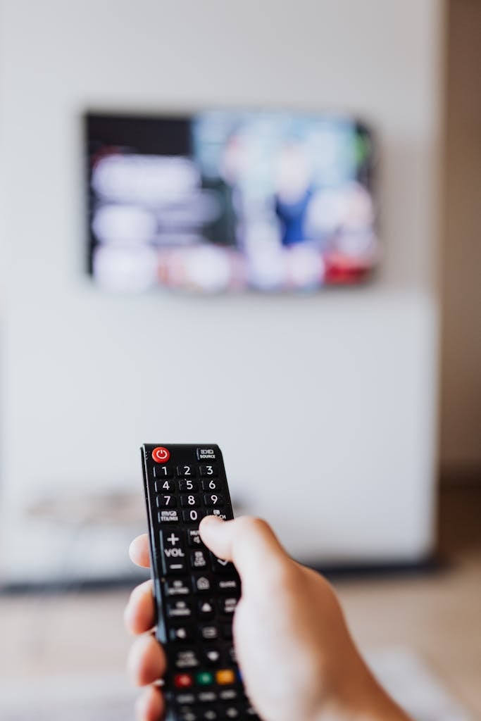 Close-up of hand using remote control to adjust a blurred television screen.