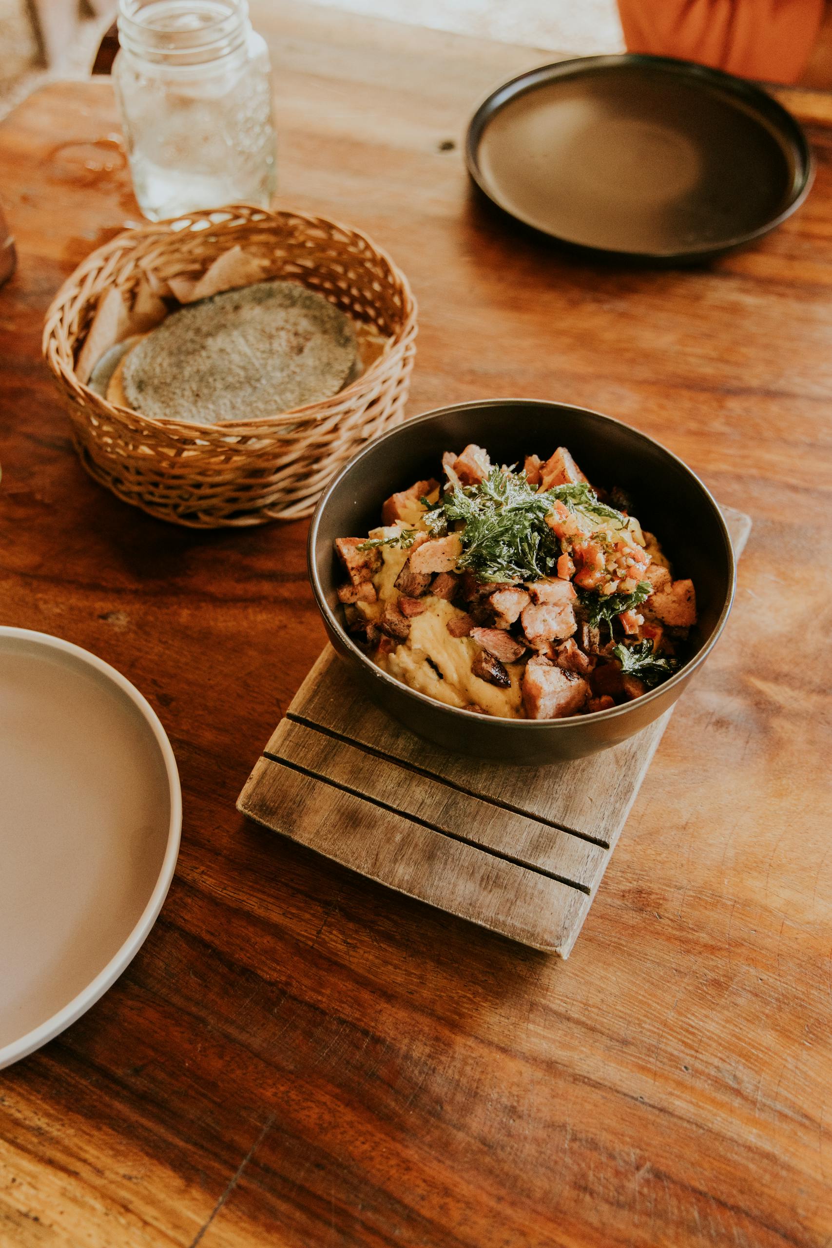 Delicious bowl of mixed dish on a rustic wooden table with bread basket and plates.