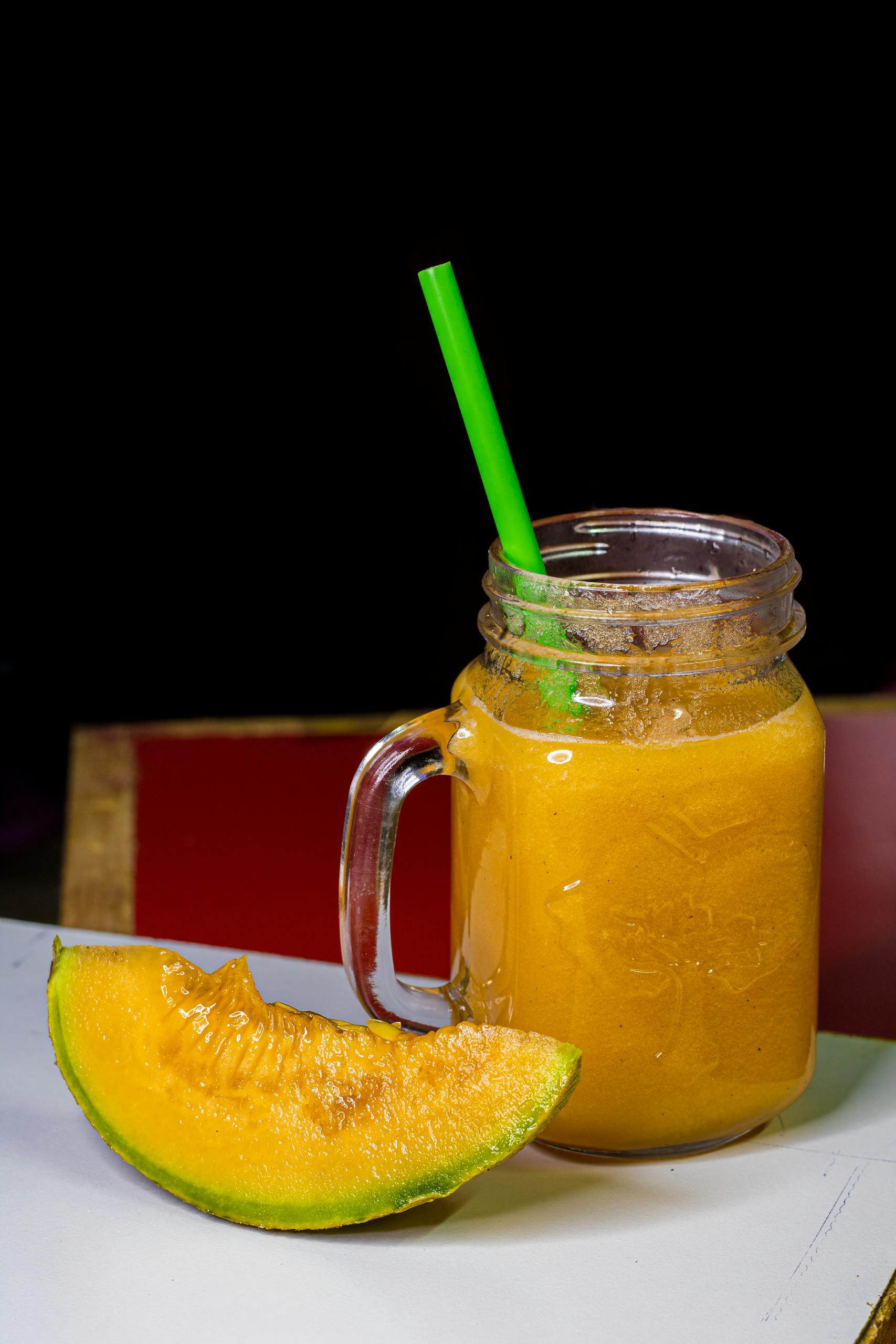 A glass mug of fresh melon juice with a green straw on a table, featuring sliced melon.