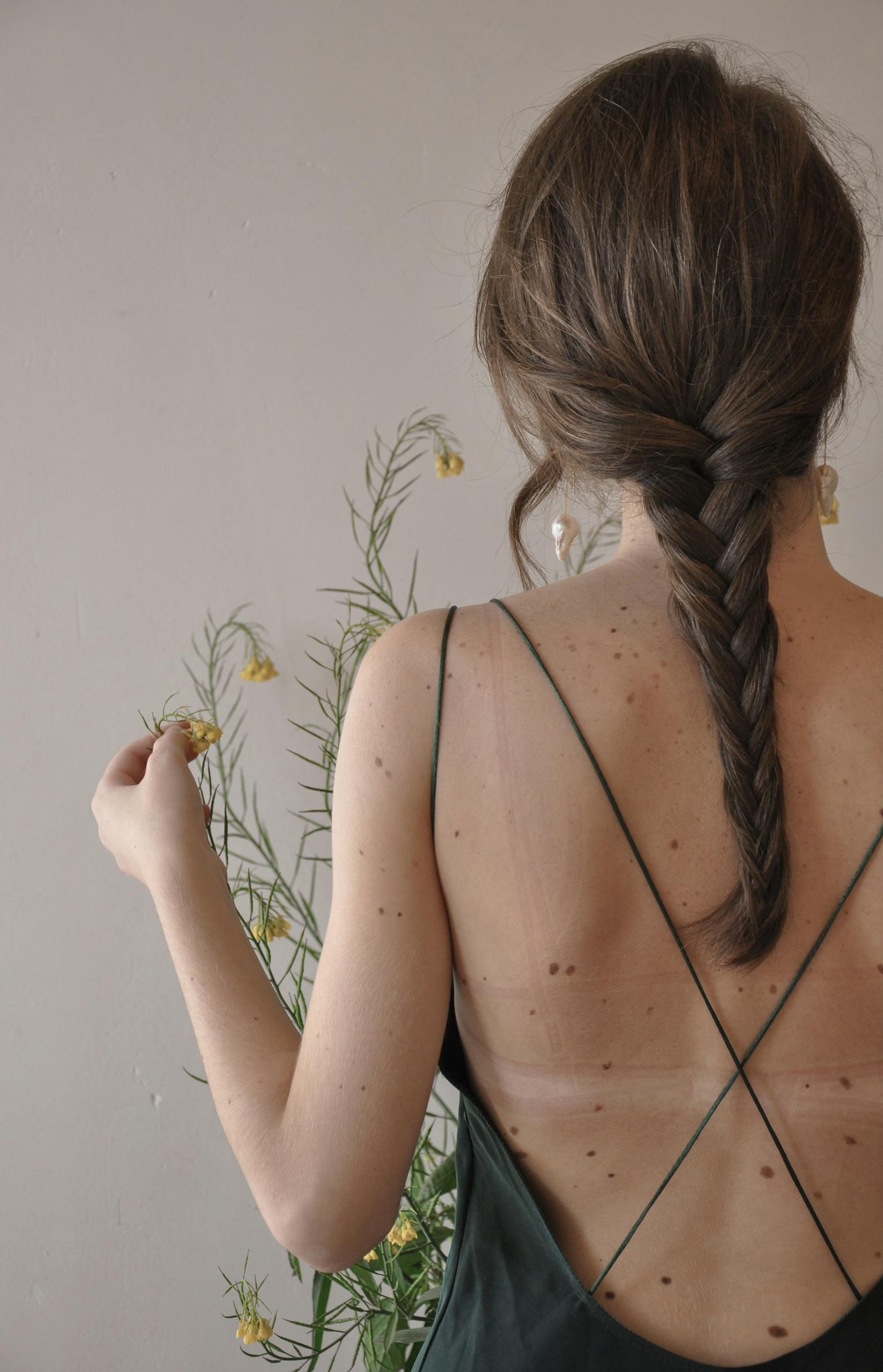 Back view of unrecognizable female with pigtail on bare skin near blooming plant