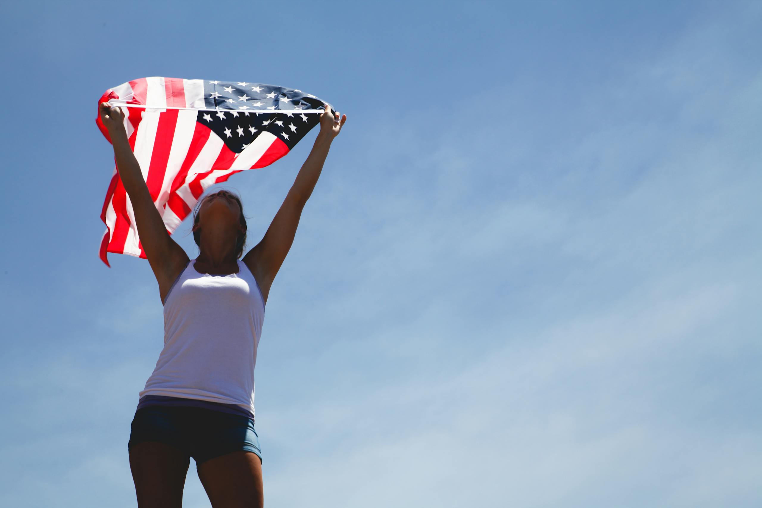 Woman celebrating Independence Day with American flag under a clear blue sky.
