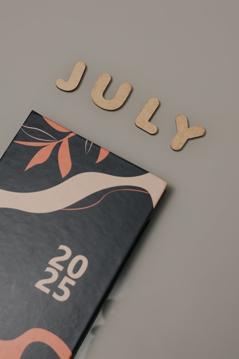 Wooden letters spelling 'July' with a 2025 planner on a neutral background.