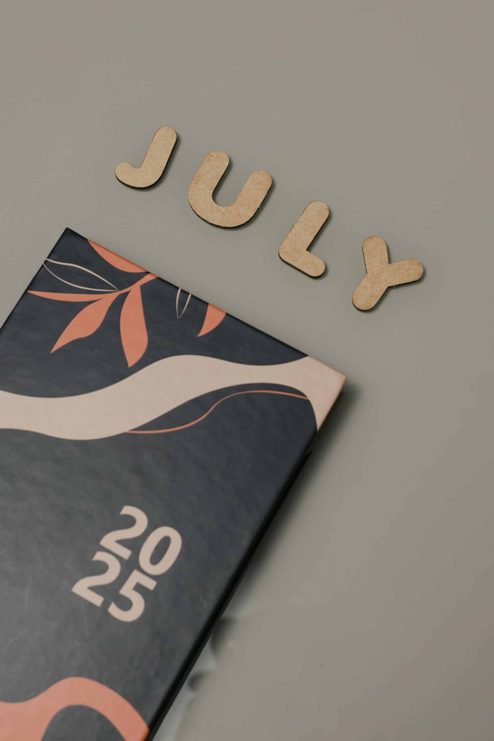 Wooden letters spelling 'July' with a 2025 planner on a neutral background.