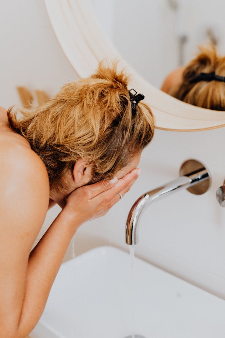 Adult woman washing her face at a bathroom sink, capturing a morning hygiene routine.