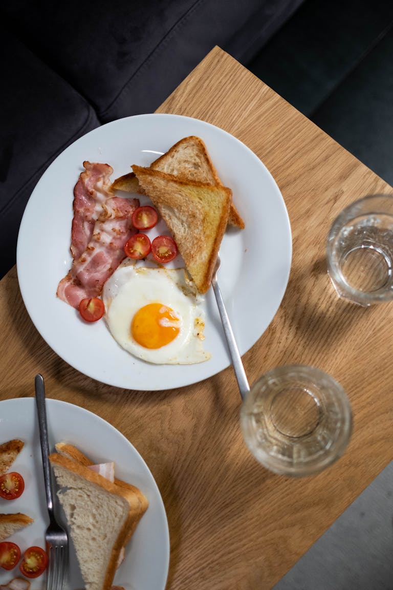 Appetizing breakfast featuring eggs, bacon, toast, and tomatoes on a wooden table.