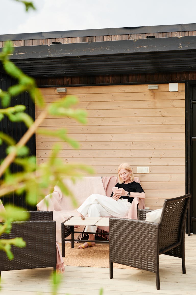 Blonde woman relaxing on modern wooden patio using a smartphone.