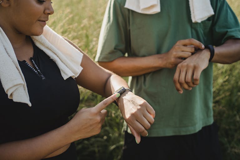 Two people checking their fitness watches while taking a break from a workout outside.