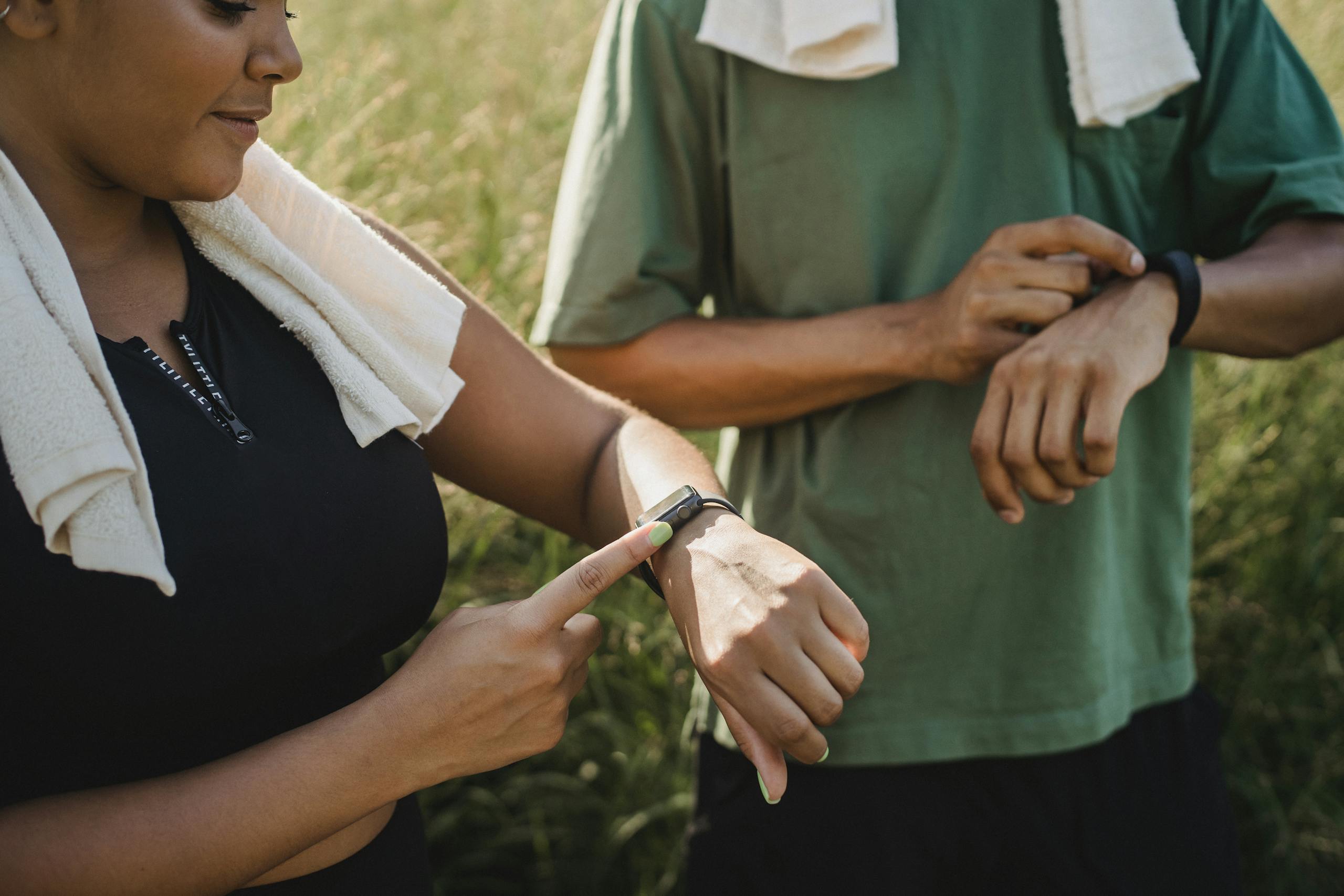 Two people checking their fitness watches while taking a break from a workout outside.