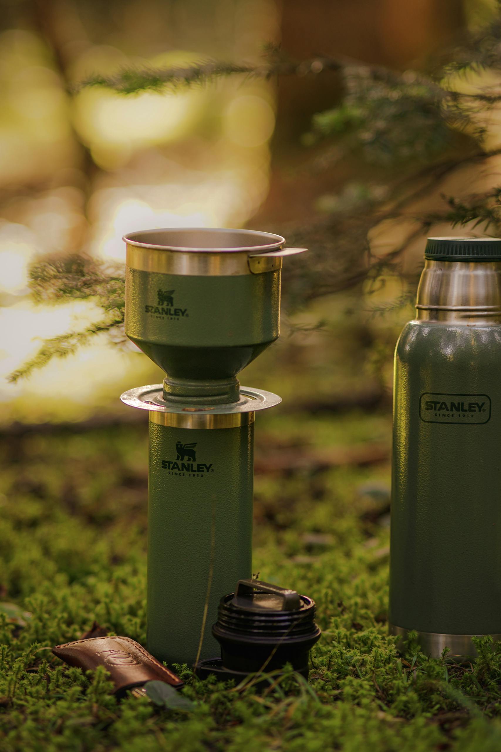 A close-up of Stanley camping gear set on moss-covered ground, ideal for outdoor adventures.