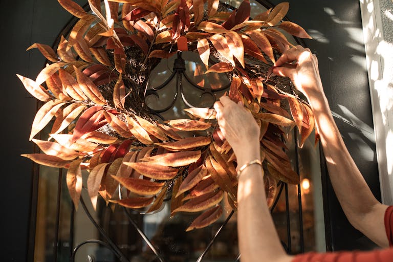 A person adjusting a decorative autumn wreath on a front door, capturing the fall atmosphere.