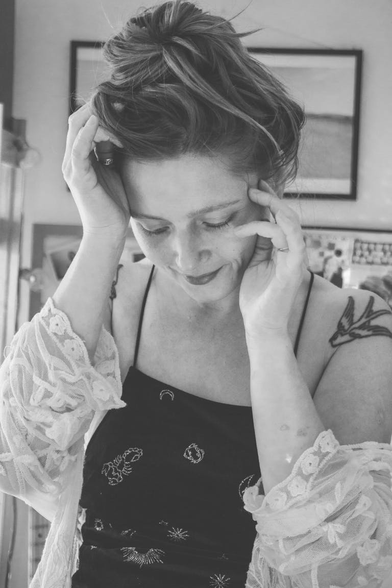 A serene black and white portrait of a young woman with tattoos indoors.