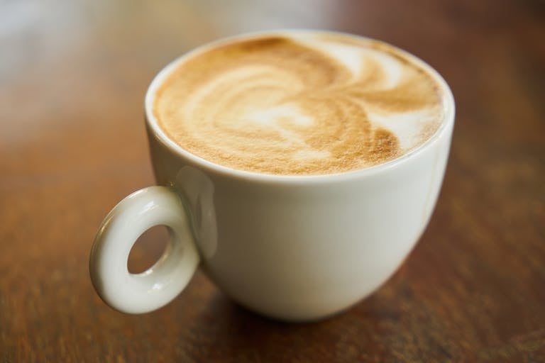 Close-up of a latte with art in a white cup on a wooden table.