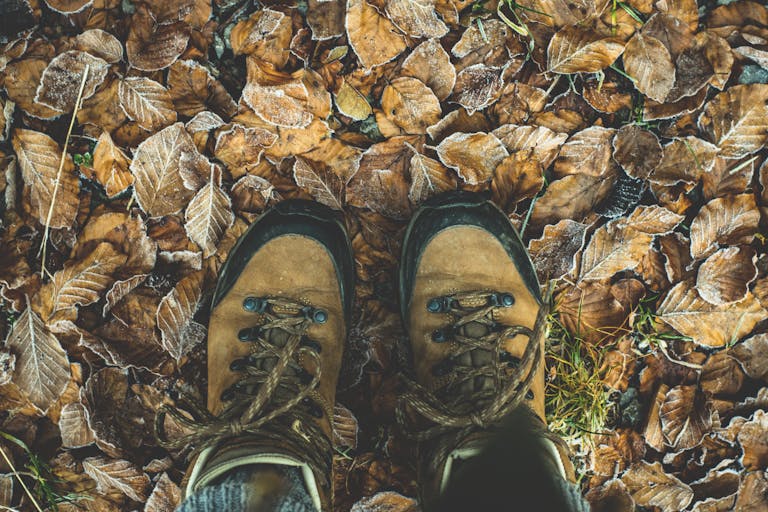 Close-up of hiking boots on frost-covered fallen leaves in autumn, capturing the essence of outdoor adventure.