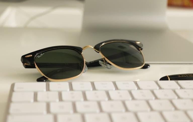 Close-up of stylish sunglasses on a desk with a keyboard, ideal for business and fashion themes.