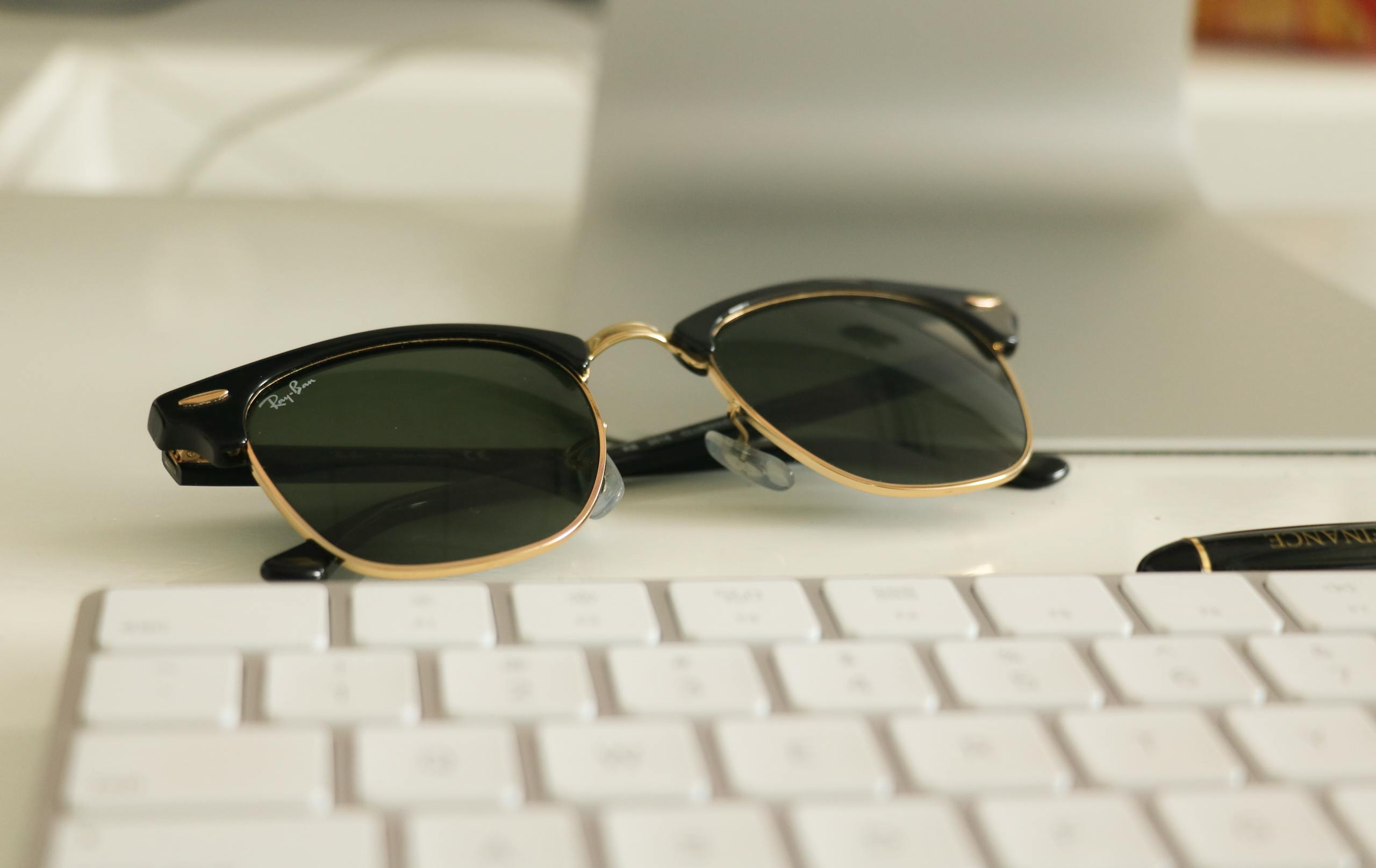 Close-up of stylish sunglasses on a desk with a keyboard, ideal for business and fashion themes.