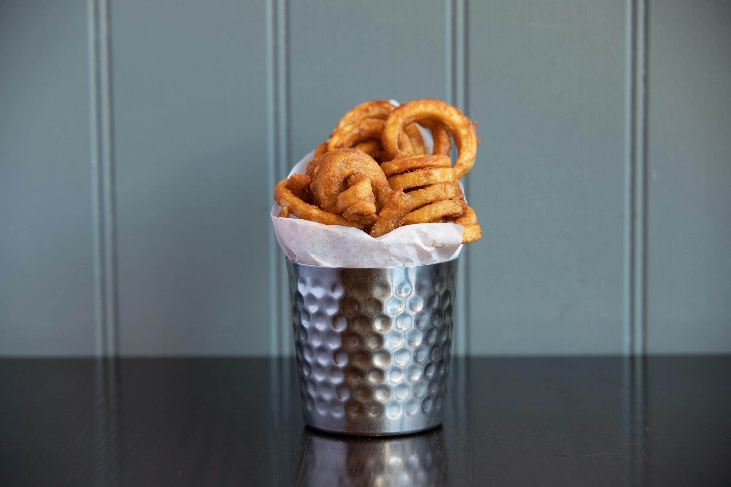 Delicious crispy curly fries served in a metal cup, perfect snack for any occasion.