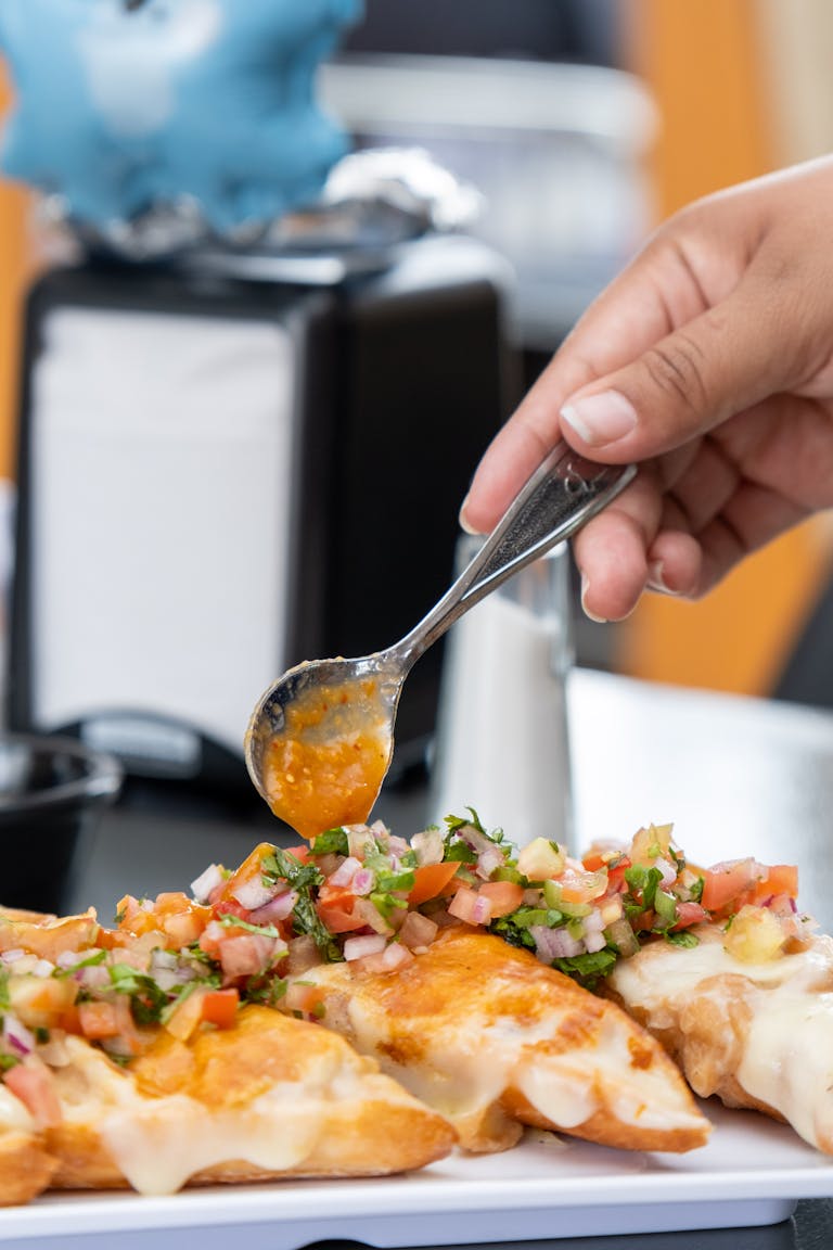 Hand spooning fresh salsa on cheesy quesadillas. Perfect culinary presentation showcasing vibrant Mexican flavors.