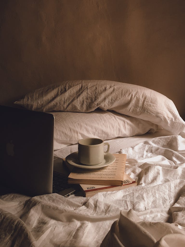 Relaxed bedroom setup with coffee, books, and a laptop on a bed, evoking comfort and leisure.