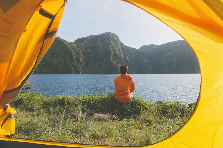 Serene view of a woman in a yellow tent, overlooking a picturesque lake and mountains in T'boli, Philippines.