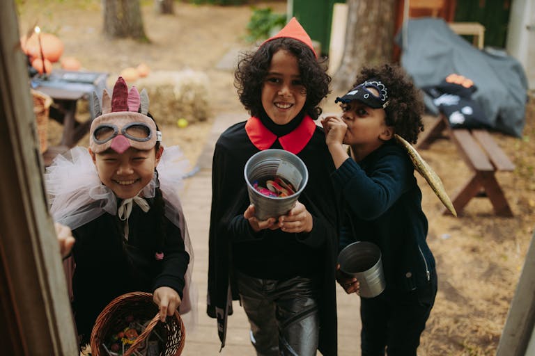 Three children in Halloween costumes joyfully trick-or-treating with candy buckets.