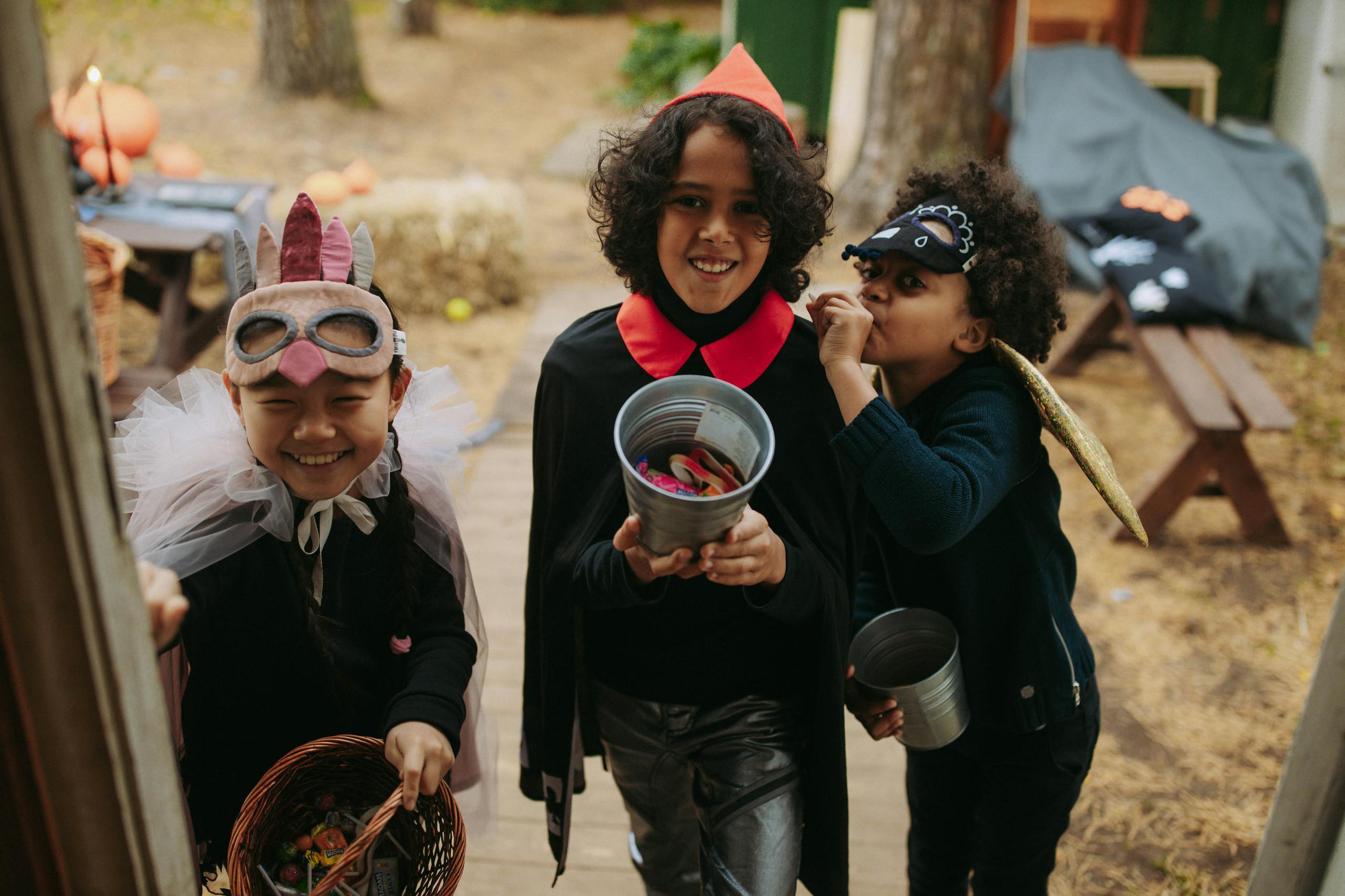 Three children in Halloween costumes joyfully trick-or-treating with candy buckets.