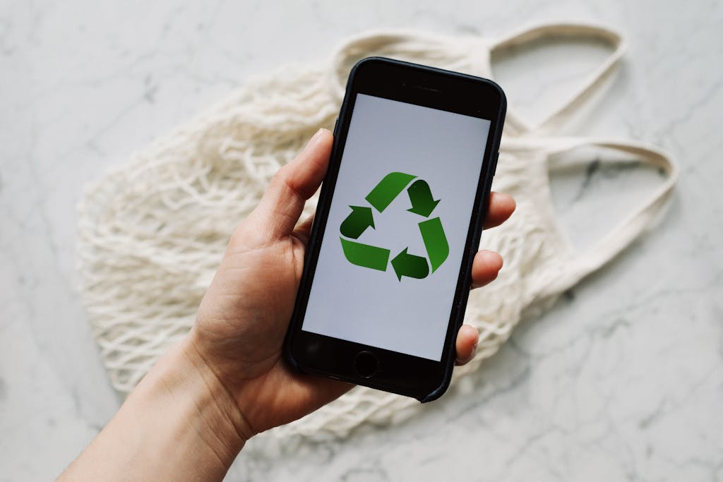 A hand holding a smartphone with a recycle symbol, emphasizing eco-friendly technology.