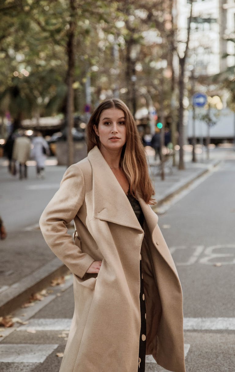 A stylish woman poses confidently in a beige trench coat on a city street.