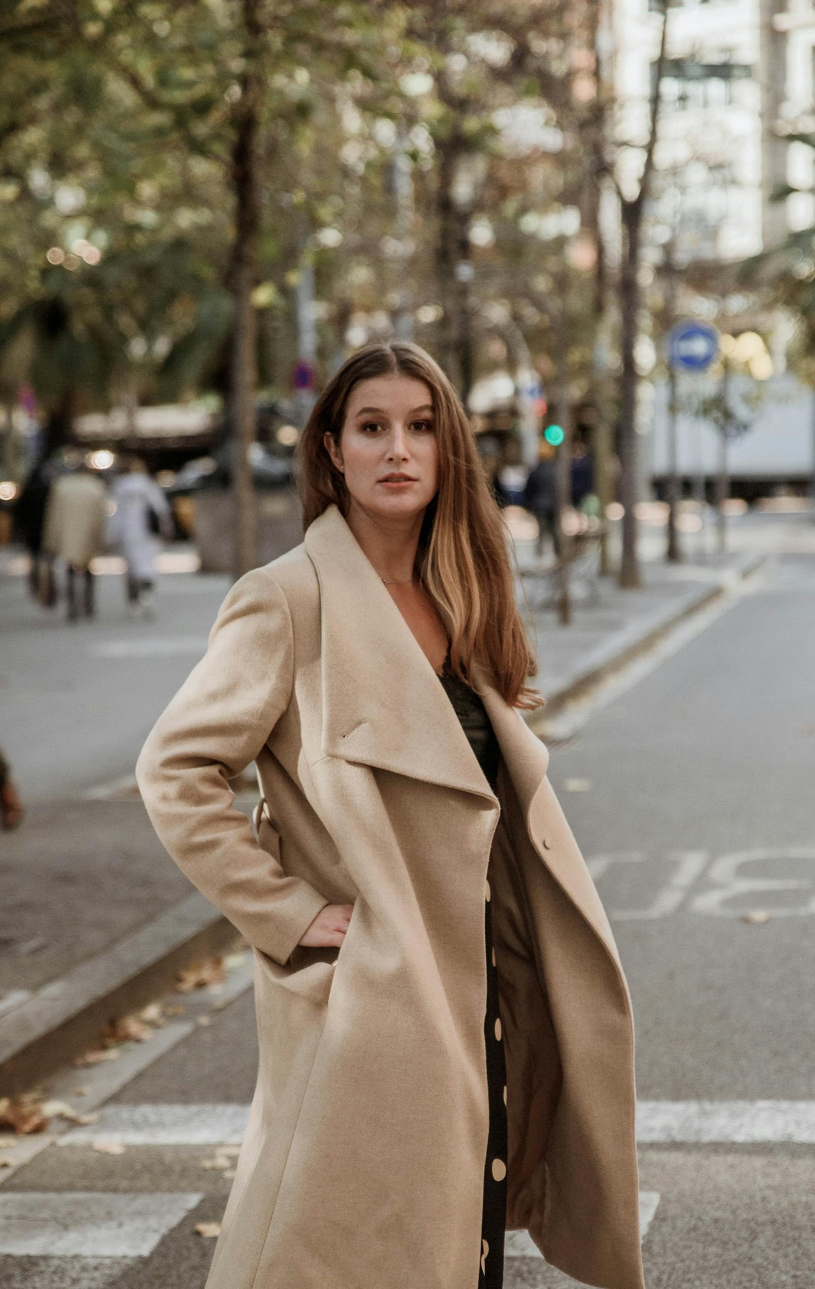 A stylish woman poses confidently in a beige trench coat on a city street.