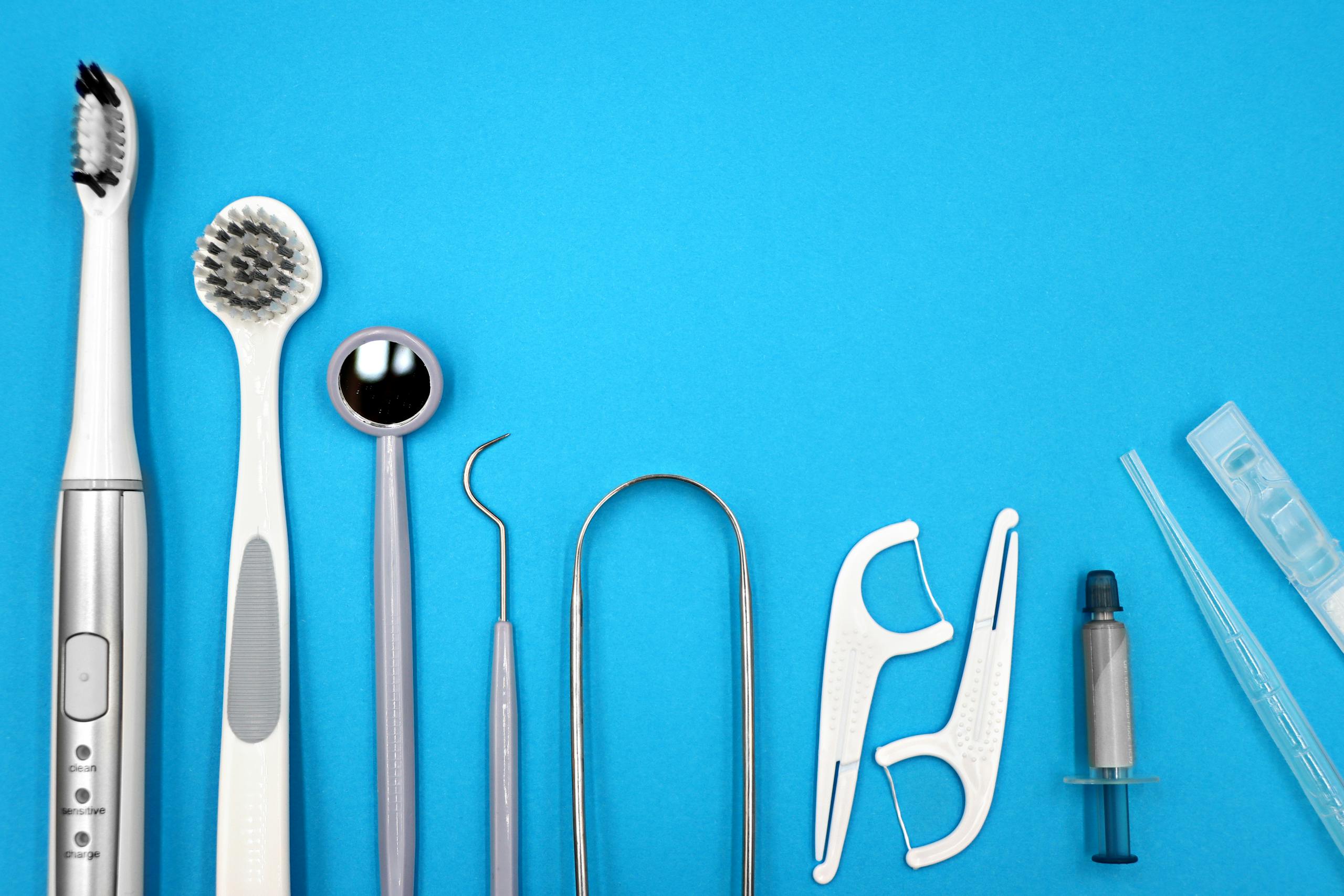 Flat lay of dental care tools including toothbrushes, dental mirror, and floss sticks on blue background.