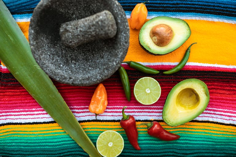 Top view of fresh ingredients for Mexican cuisine, including avocados, chilies, limes, and a mortar.