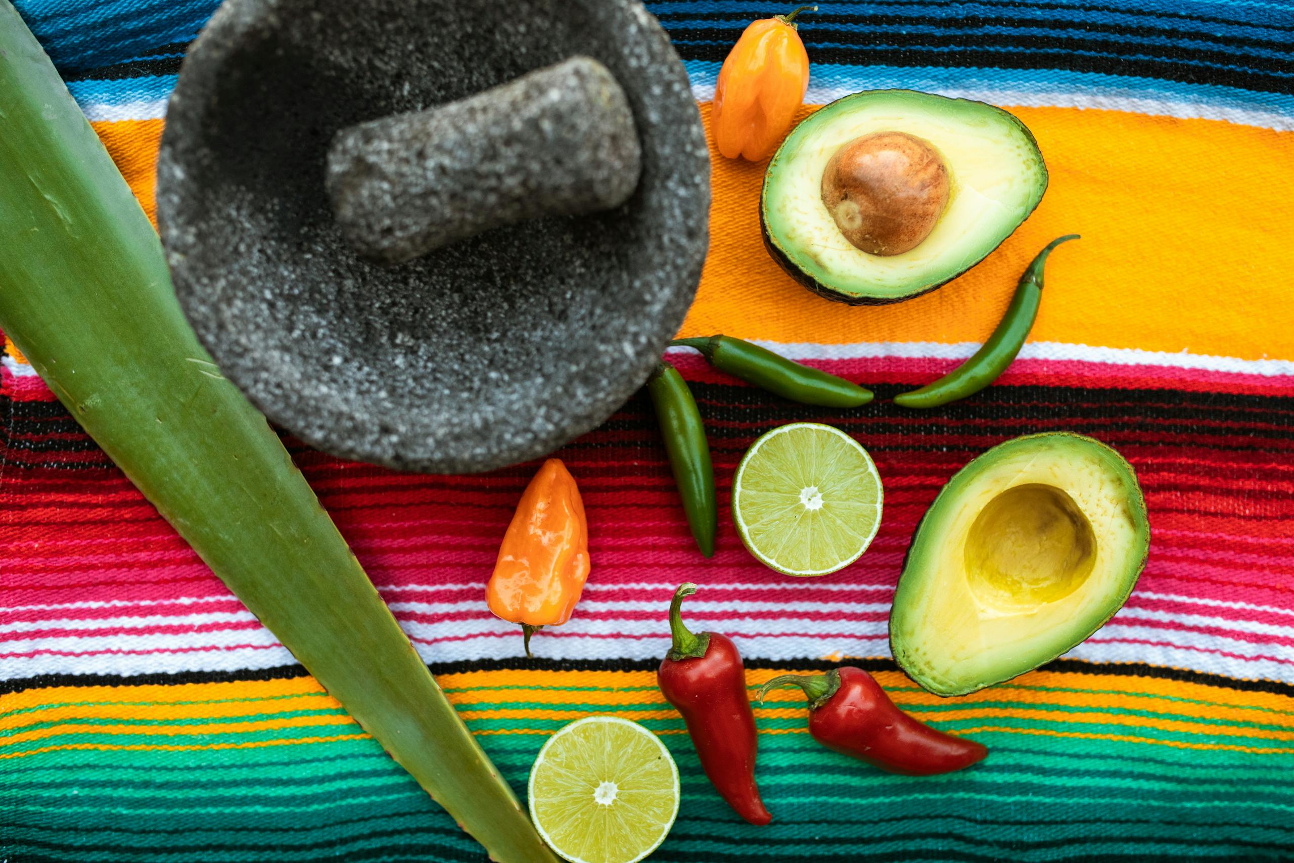 Top view of fresh ingredients for Mexican cuisine, including avocados, chilies, limes, and a mortar.