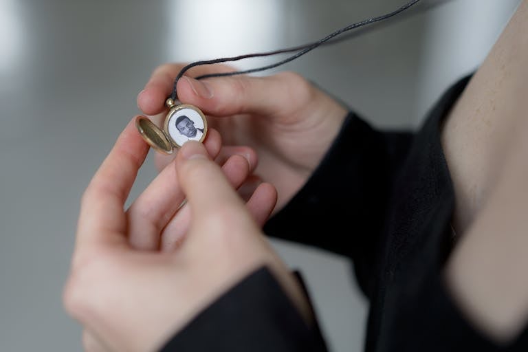 A detailed view of hands holding an antique locket with a black and white photo inside.