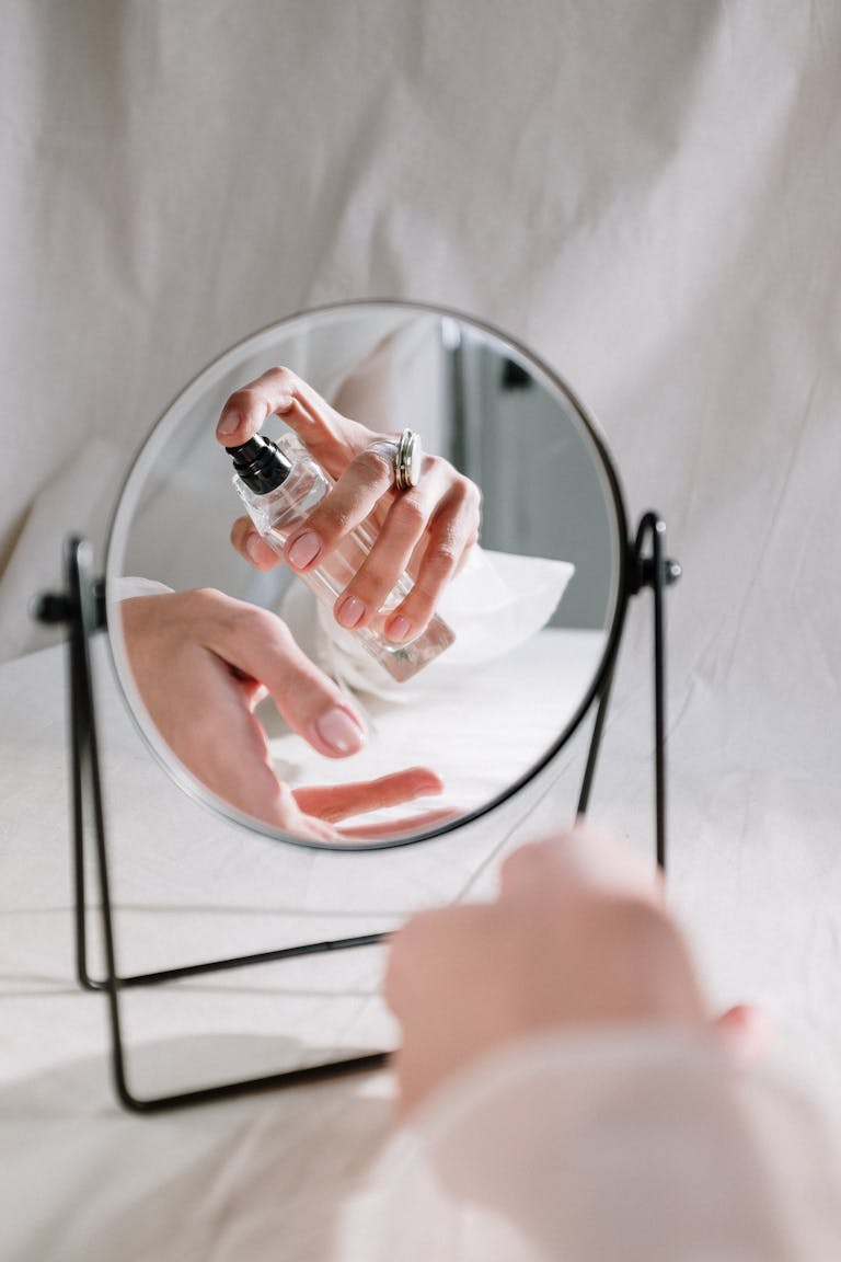 A graceful hand holding a perfume bottle reflected in a mirror, creating an elegant scene.
