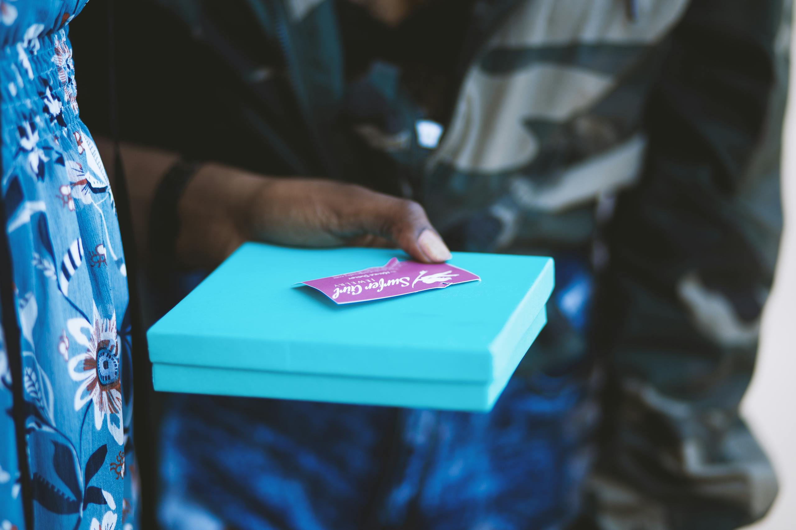 A detailed view of hands holding a blue gift box with a card indoors.