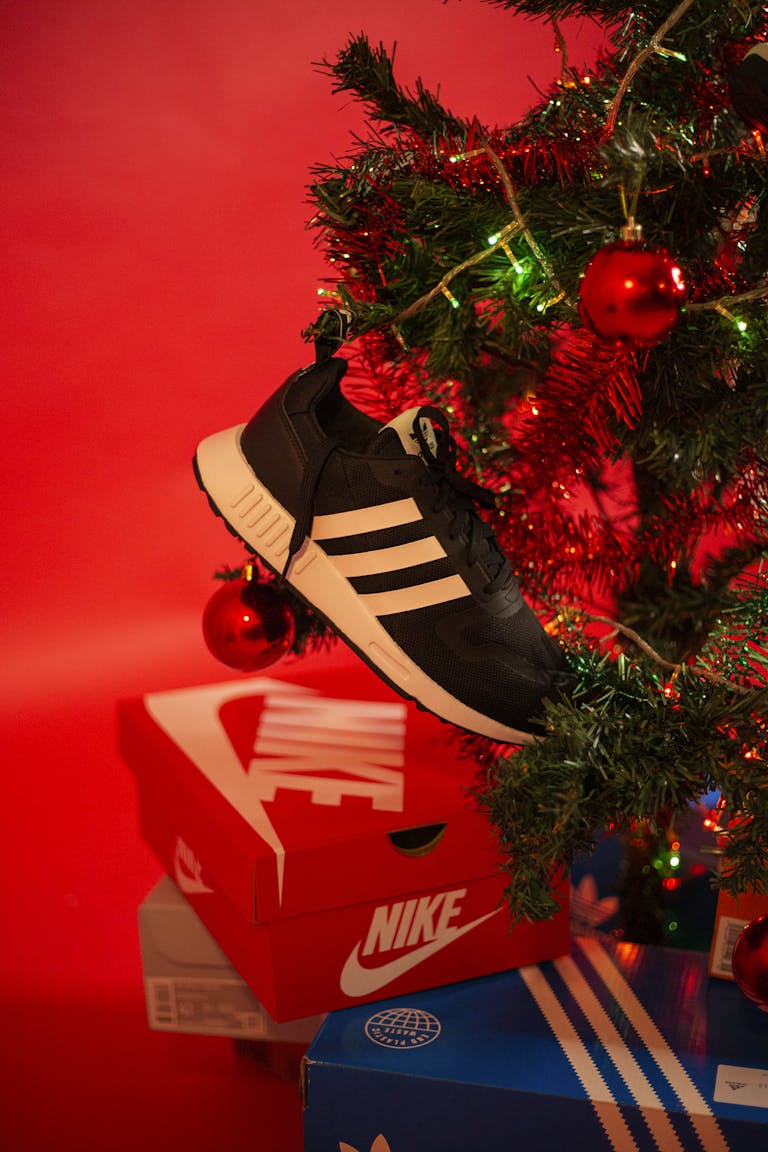 A stylish sneaker hanging by a decorated Christmas tree with gift boxes below.