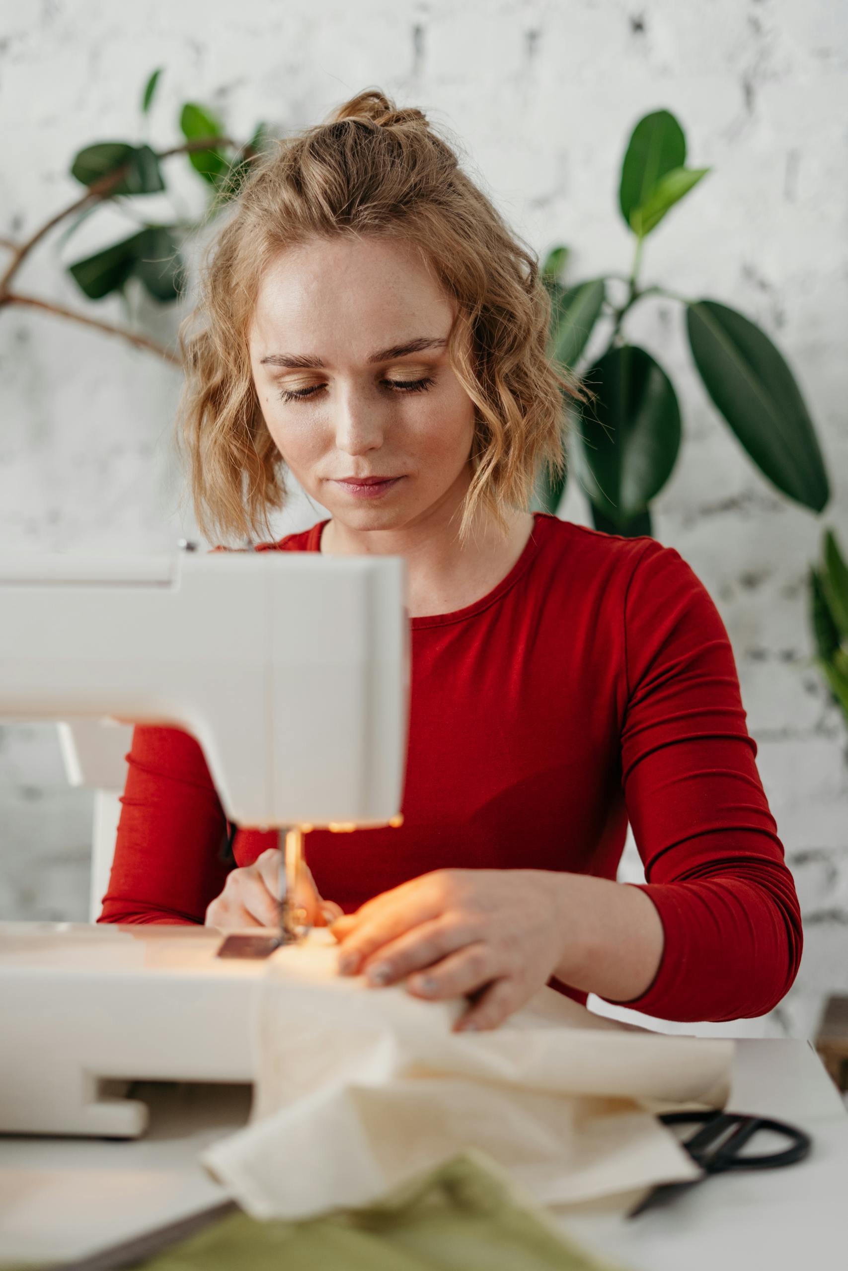A young woman in a red dress sewing fabric indoors, showcasing creativity and craftsmanship.