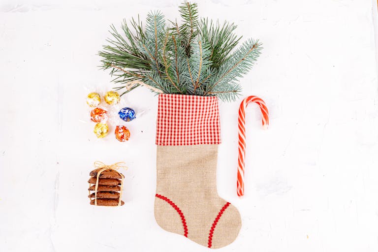 A festive Christmas stocking filled with pine branches, candy canes, cookies, and chocolates on a white background.