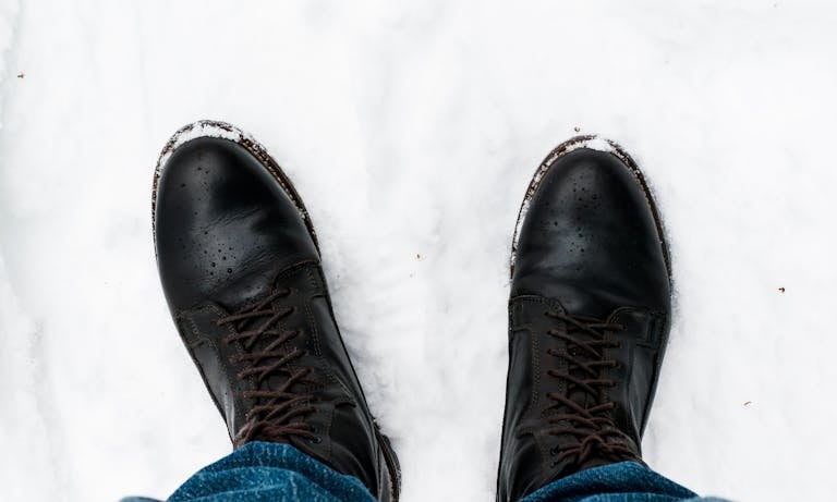 A pair of black leather boots stand in fresh snow, captured in Oslo during winter.