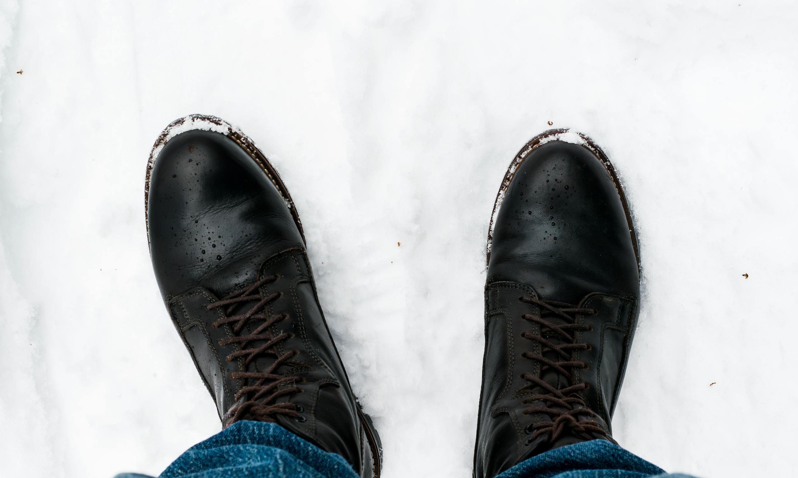 A pair of black leather boots stand in fresh snow, captured in Oslo during winter.