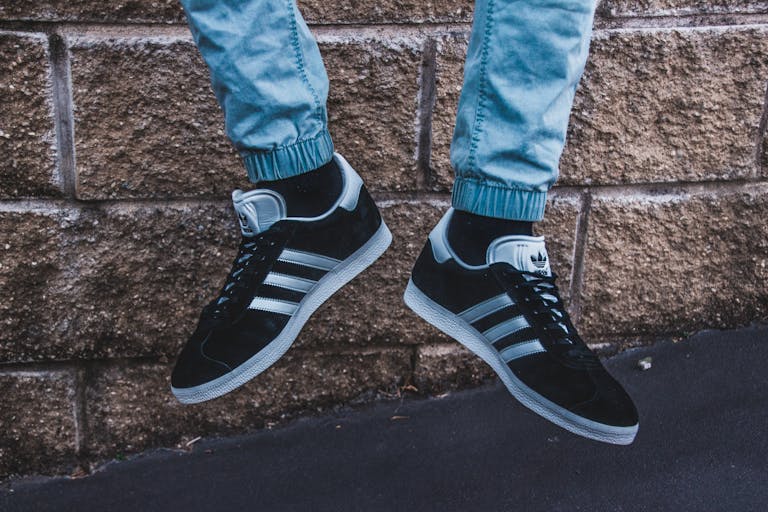 Close-up shot of Adidas sneakers and denim jeans against a brick wall, showcasing urban street style.