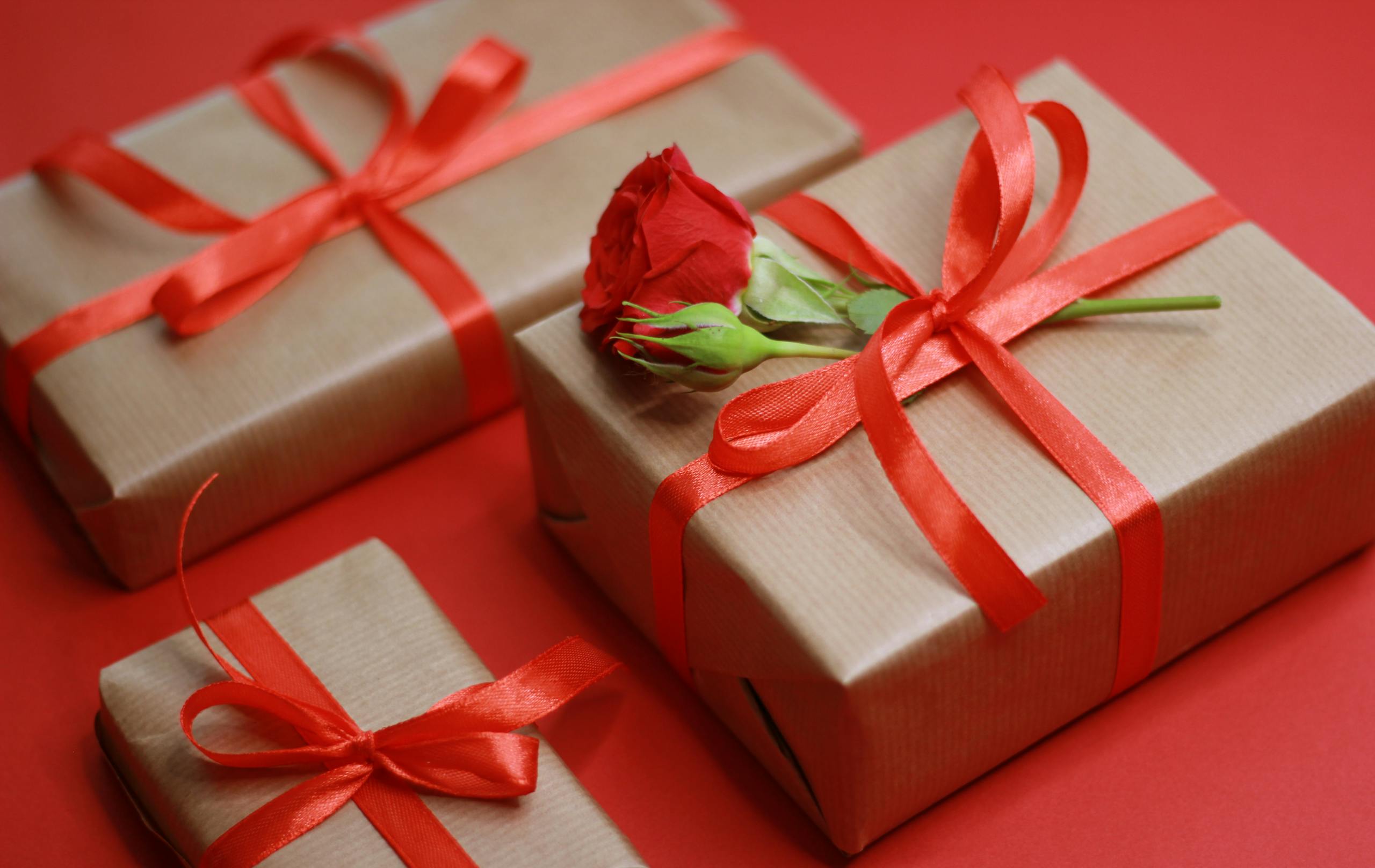 Elegant gift boxes tied with red ribbons and a rose on a red background.