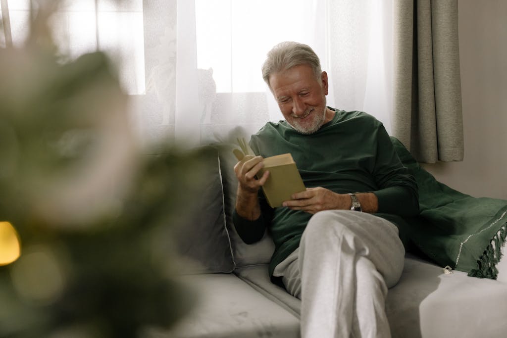 Senior man relaxing and reading a book on a sofa, enjoying the cozy holiday atmosphere indoors.