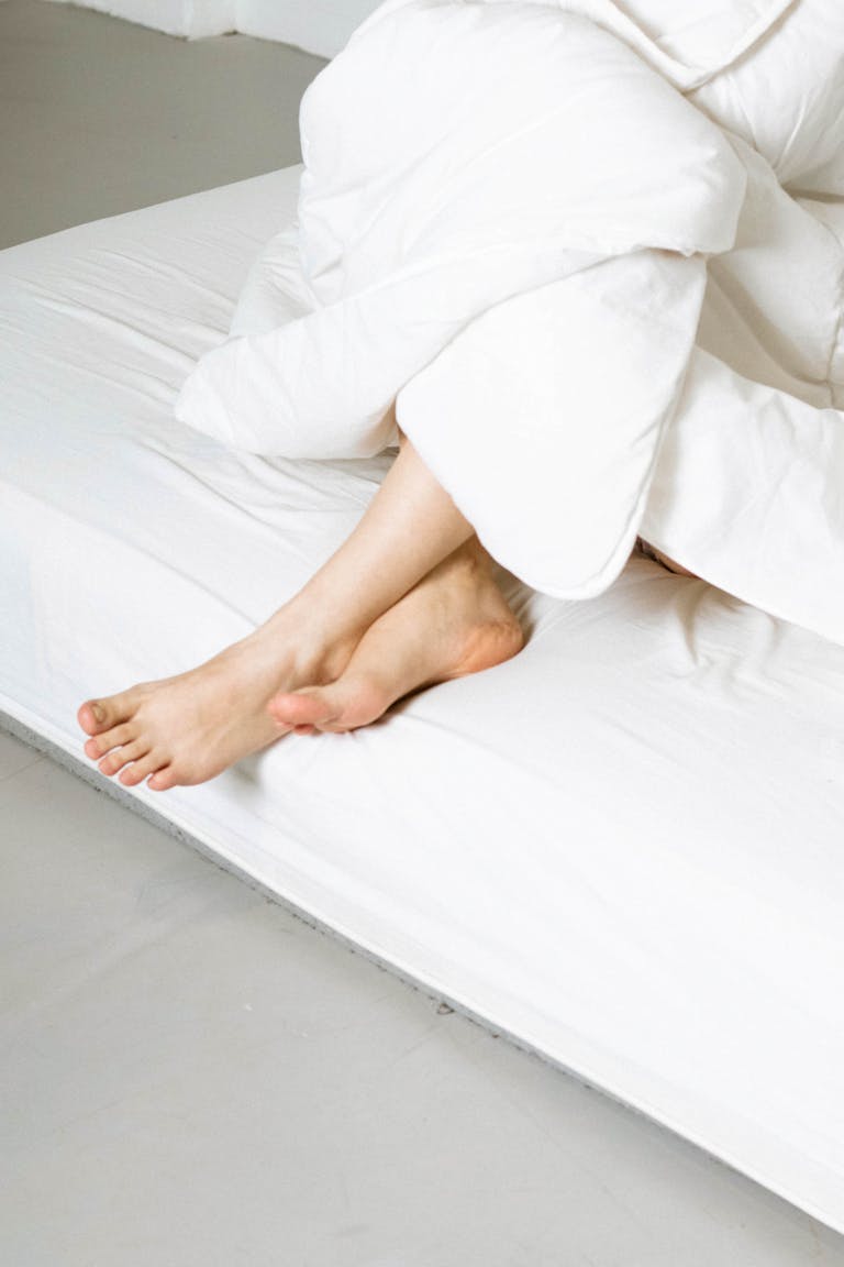 A peaceful scene of bare feet resting on a bed, wrapped in cozy white bedding.