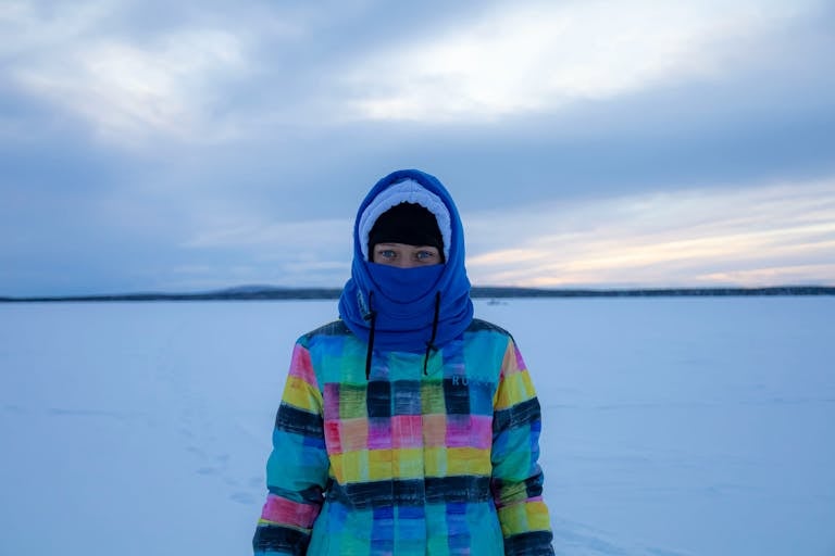 A person bundled in a colorful winter jacket stands in a snow-covered landscape during the day.