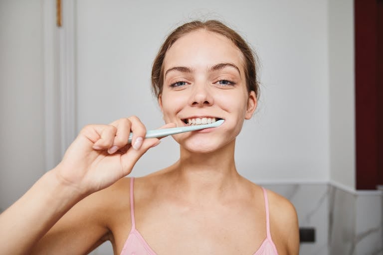 Close-up of a woman smiling while brushing teeth in a modern bathroom.