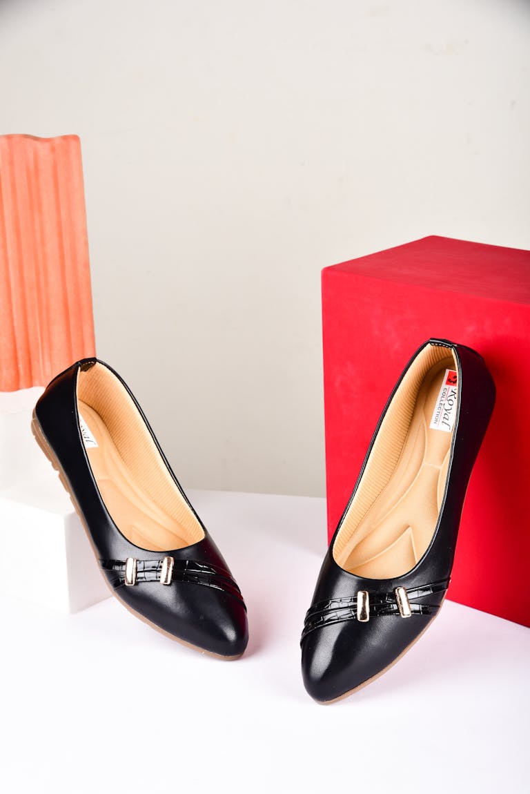 Sophisticated black women's flats on minimalist white and red background, perfect for modern fashion photography.