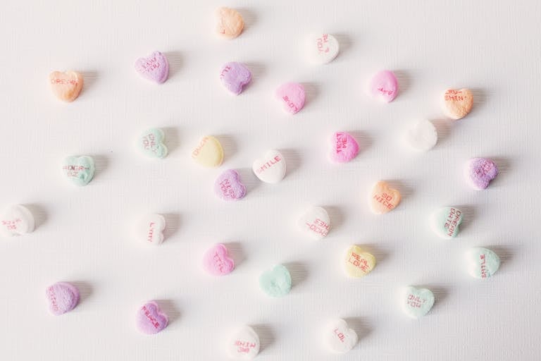 Top view composition of multicolored small heart shaped sweets placed on plain white surface