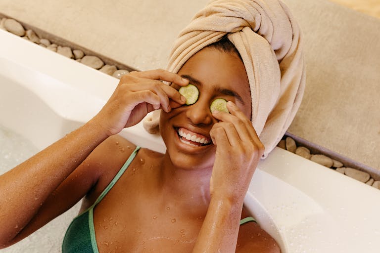 Woman enjoying a spa bath with cucumber slices on eyes, embracing relaxation.