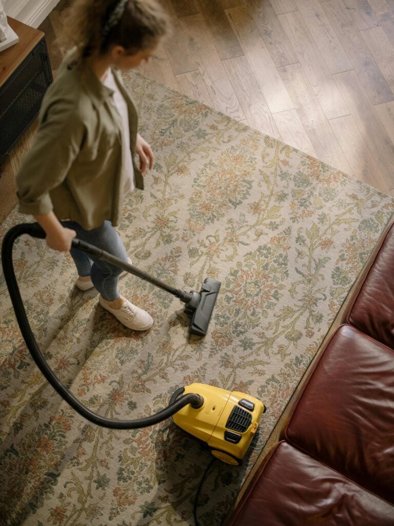 Overhead view of a woman vacuuming a carpet at home, highlighting cleanliness and housekeeping.