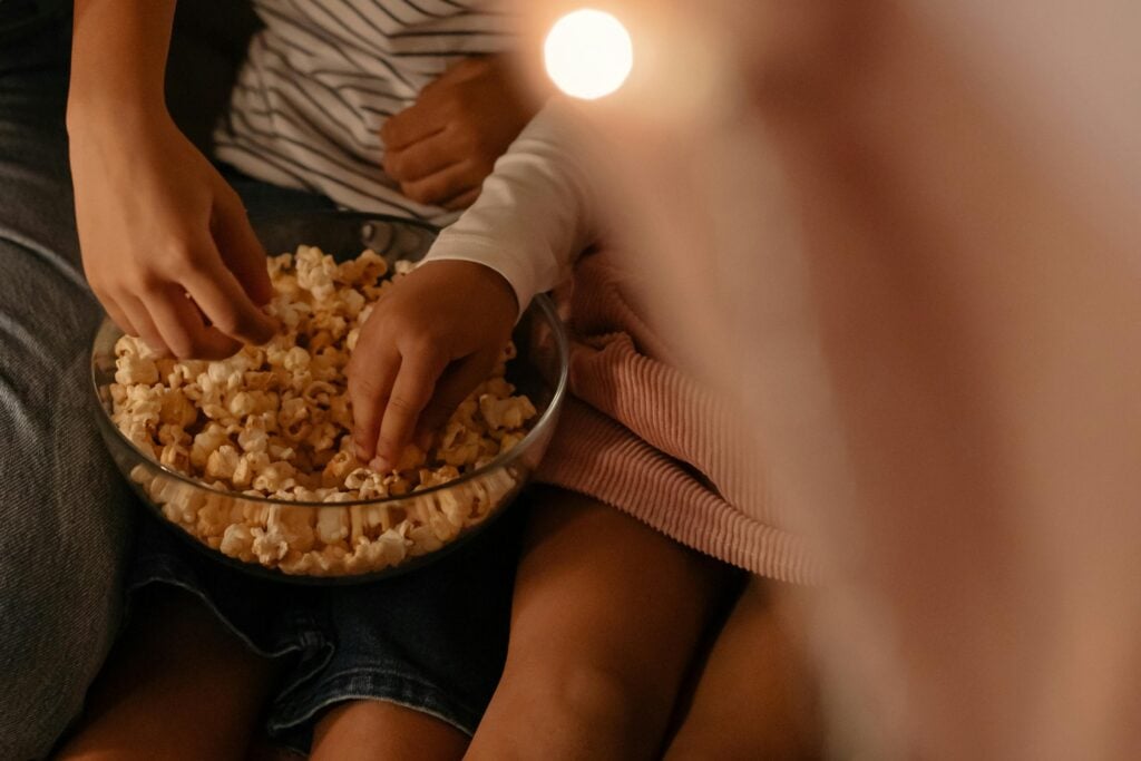 Two children sharing a bowl of popcorn indoors with a warm, cozy atmosphere.